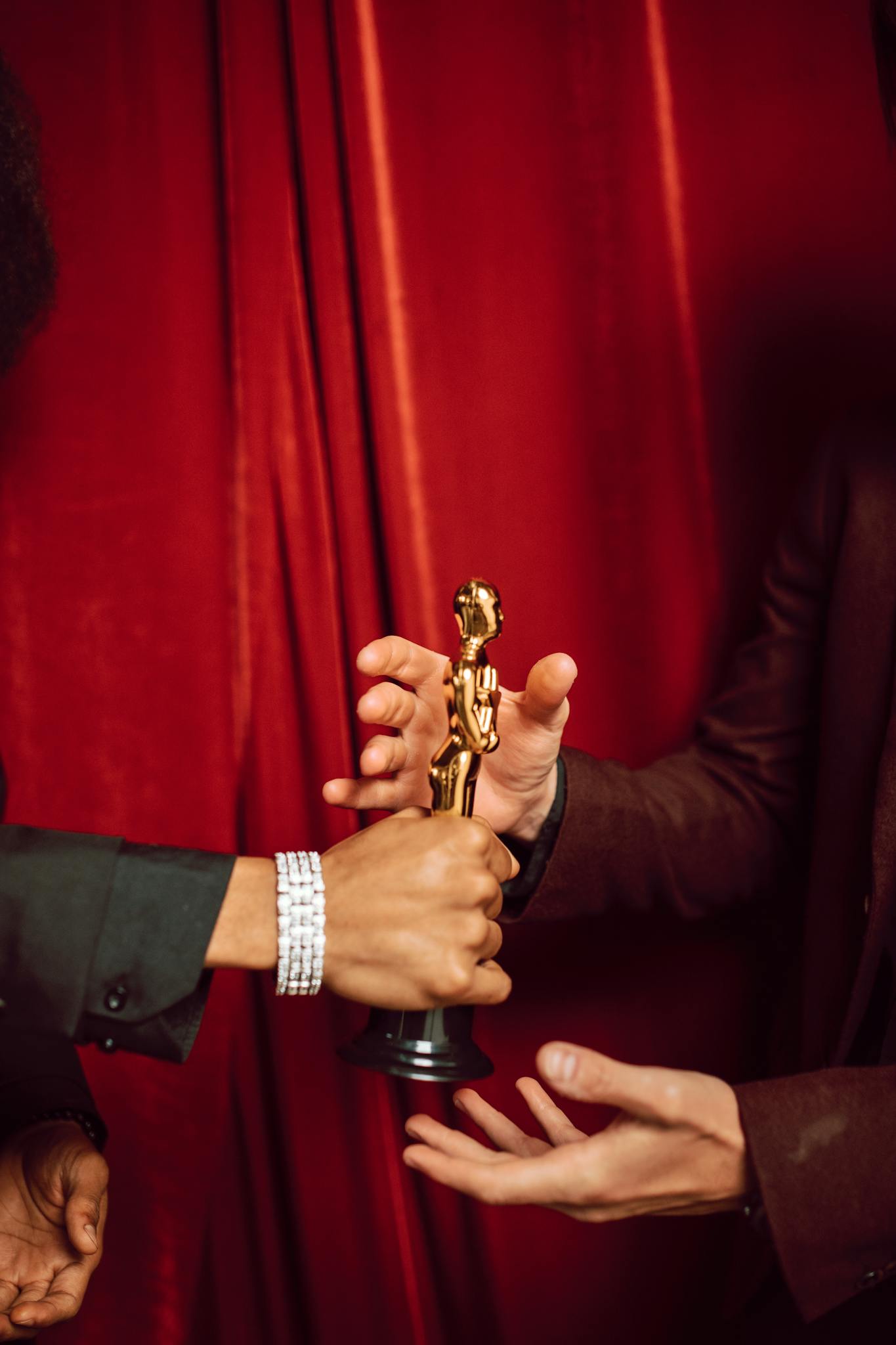 Close-up of two people exchanging a golden trophy in front of red curtains.